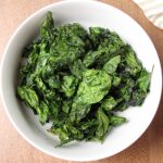 Bowl of air fried spinach chips with a sprinkling of salt.