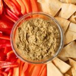 Baba ganoush in a bowl with pita, sliced red peppers and orange peppers.