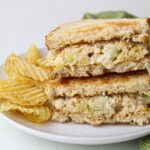 Chickpea salad on toasted bread, cut in half and stacked, with potato chips on a white plate.