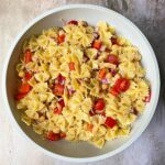 Pasta salad with red onion, peppers, tomatoes and chickpeas in a large bowl.