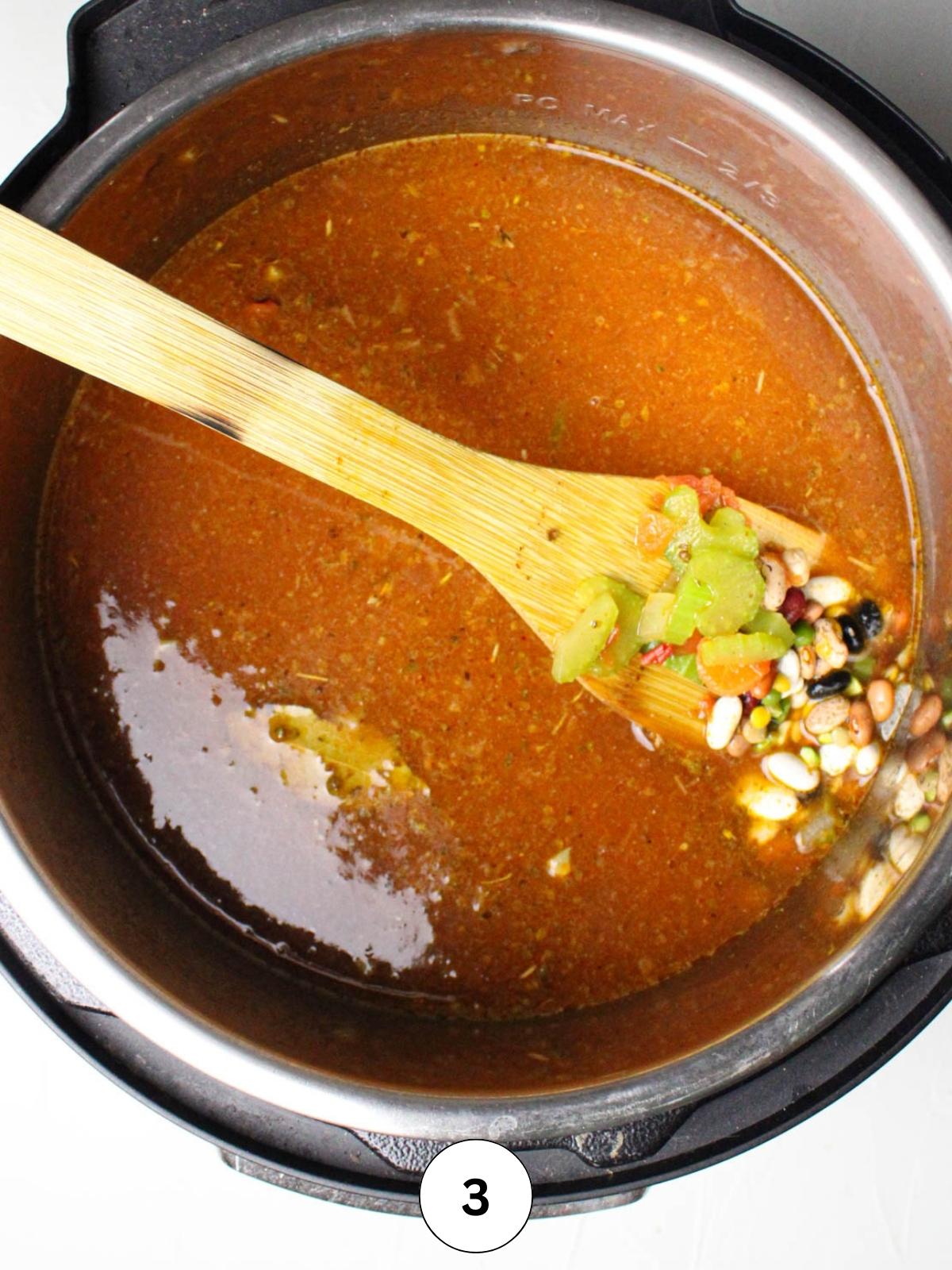 Instant Pot with broth, veggies, and beans with a wooden spatula.