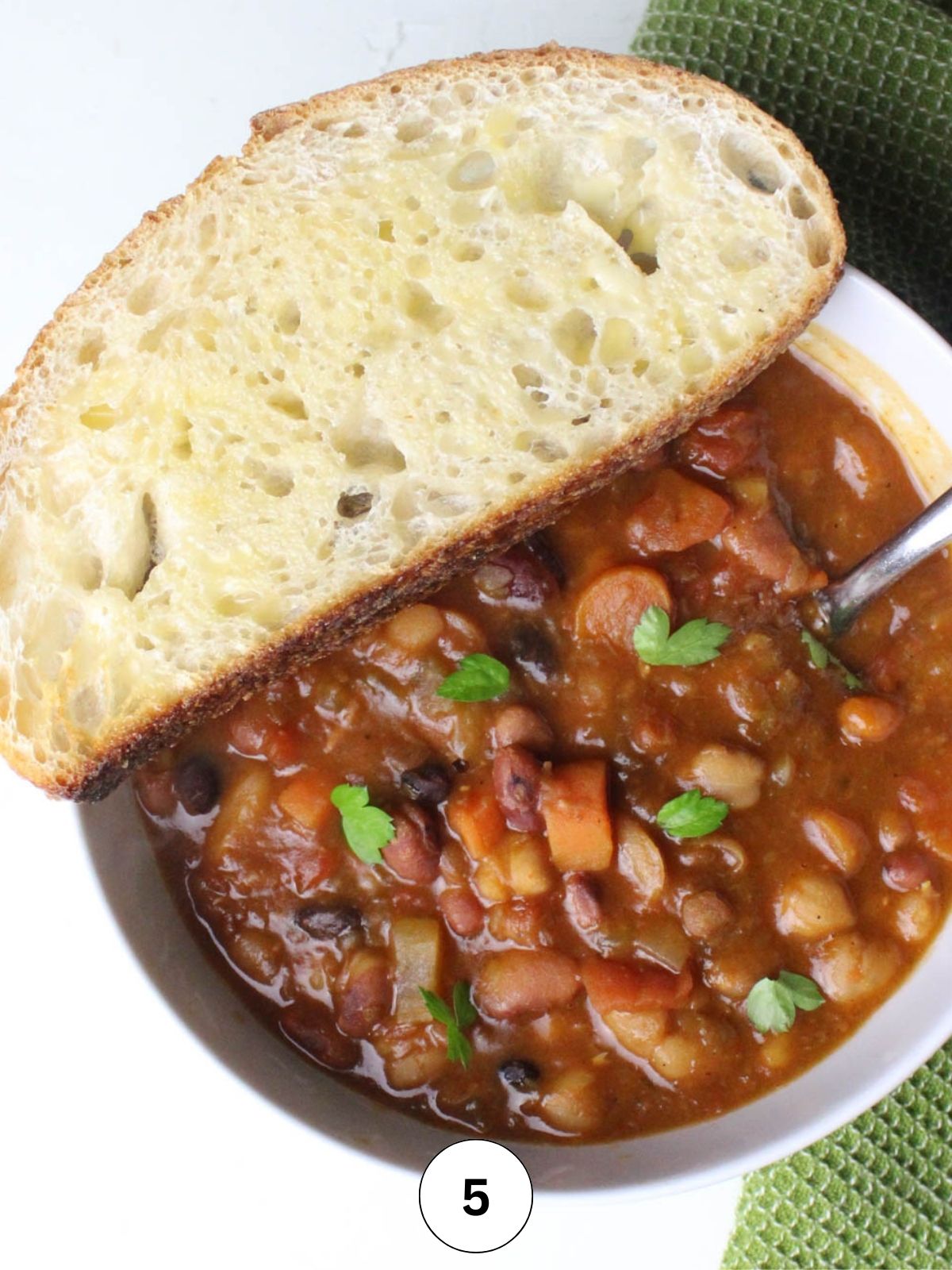 A bowl of 15 bean soup, garnished with fresh parsley, and toasted sourdough bread.